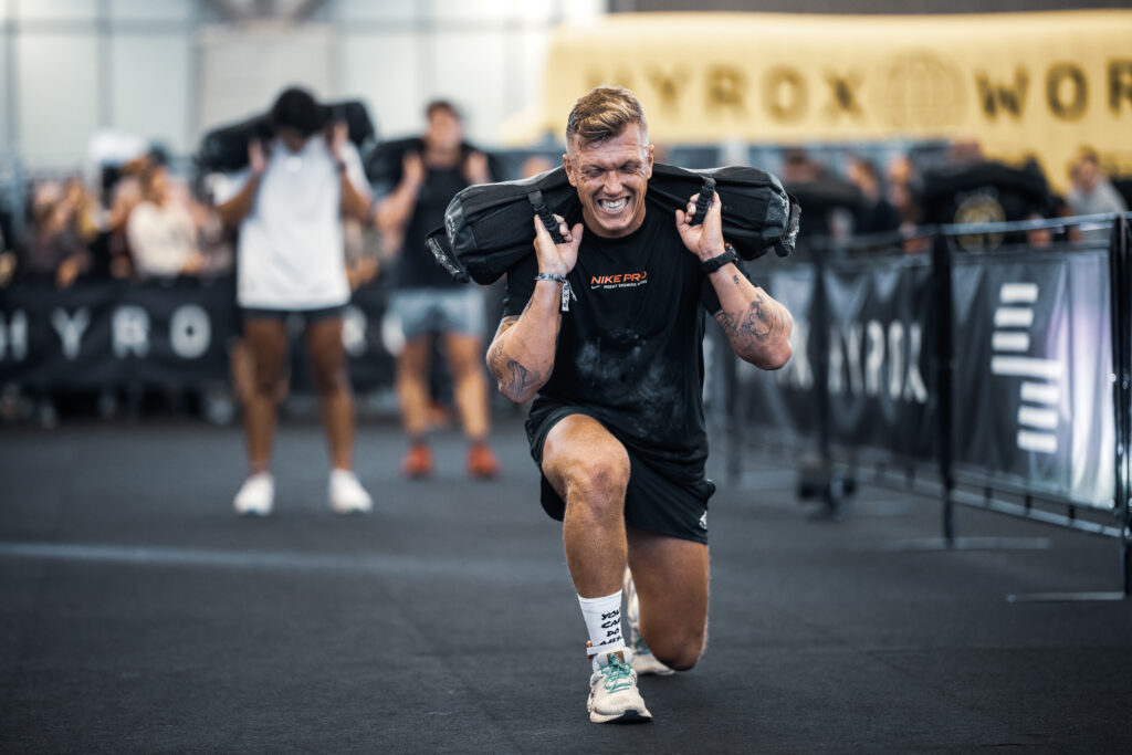 Un homme réalisant des sandbag lunges lors d'une course Hyrox.