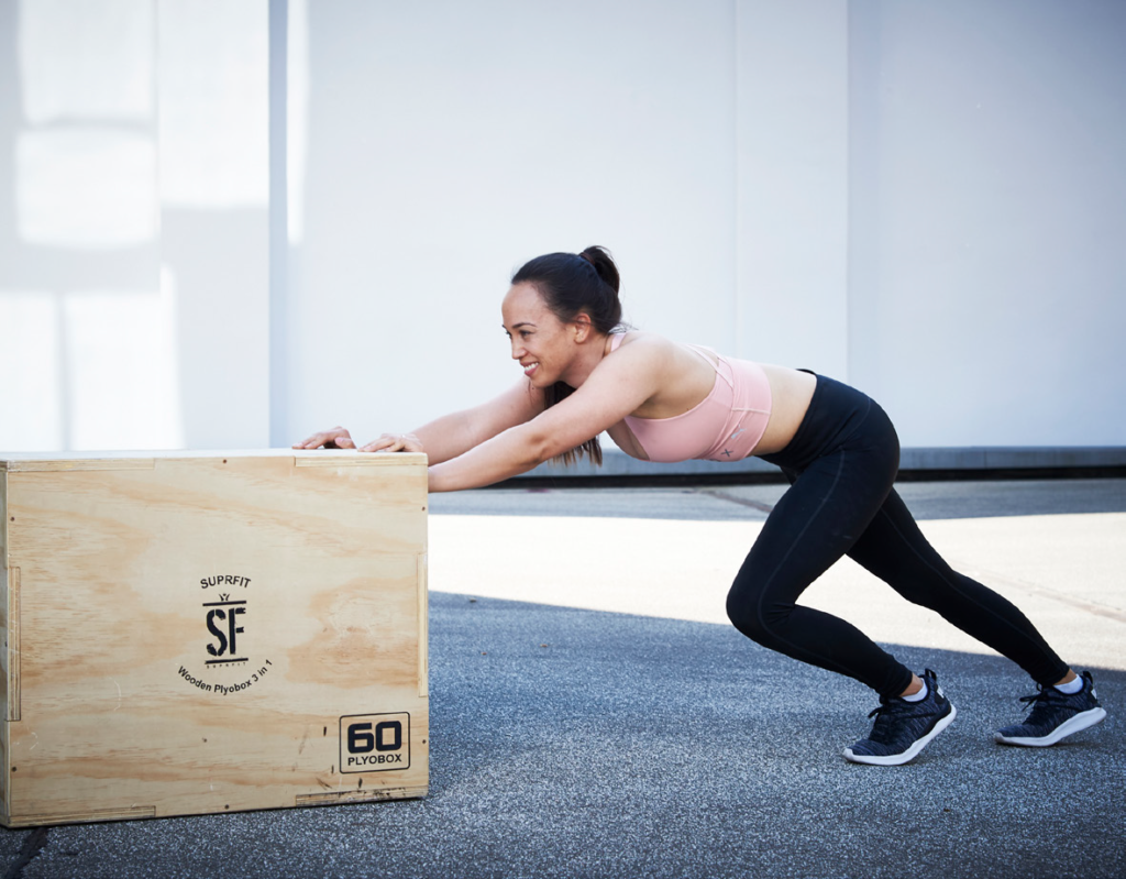 Une femme poussant une plyobox pour simuler l'effort sur le sled push.