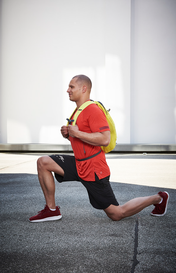 Un homme effectuant des lunges en utilisant un sac à dos lesté à la place du sandbag lors de son entraînement Hyrox.